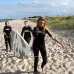 drei-kinder-tragen-ein-surfbrett-von-der-ostsee-surfschule